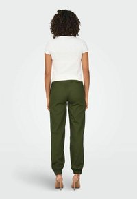 Biała, prążkowana bluzka z krótkim rękawem i zielone spodnie dresowe. Spodnie mają elastyczne mankiety, luźny krój i gładką teksturę.