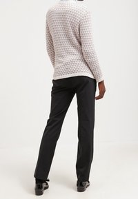 Maglione leggero a maglia con un motivo geometrico in tonalità tenui, abbinato a pantaloni slim-fit scuri, completato con scarpe lucide con lacci.