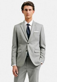 Ljusgrå kostym med en slim fit-design, slagkragar, två framfickor och en enkel knappstängning. Vit skjorta och marinblå slips ingår.