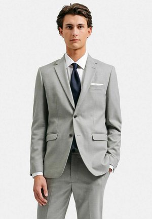 Lys grå jakkesæt med et slim fit design, notch lapels, to frontlommer og en enkelt knaplukning. Hvid skjorte og marineblå slips medfølger.