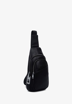 Sac en cuir noir en bandoulière avec deux compartiments zippés et une sangle réglable, sur fond blanc.