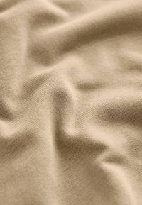 Beige Baumwollstoff mit einer weichen, glatten Textur, die in sanften Falten präsentiert wird und ein feines Strickmuster sowie einen subtilen Glanz zeigt.