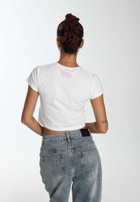 White cropped t-shirt with pink back print and short sleeves, paired with high-waisted light blue denim jeans featuring back pockets.