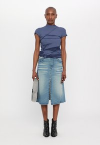 Marineblå tætsiddende top med diagonal tekstureret design, lyseblå denim A-line nederdel med slids foran, sorte ankelstøvler og en perlebesat clutch.