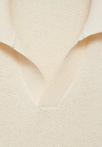 Cream-colored knitted sweater featuring a textured surface, a V-neck design, and contrasting smooth fabric at the collar and cuffs.