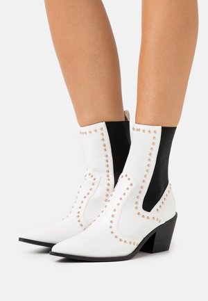 Botas de tobillo de imitación cuero blancas con lados elásticos negros, detalles de tachuelas, punteras puntiagudas y un tacón corto y negro.