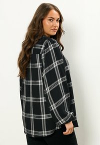 Camicia a quadri bianca e nera con un taglio morbido, maniche lunghe e polsini con bottoni. Presenta un colletto e un tessuto morbido e testurizzato.