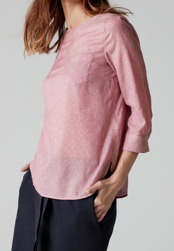 Ljust rosa blus med ett strukturerat mönster, trekvartslånga ärmar, en bröstficka och sidofickor. Tillverkad av ett genomskinligt, mjukt tyg.