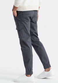Grå cargo bukser med elastiske manchetter, sidelommer og en afslappet pasform, parret med hvide sneakers for et afslappet look.