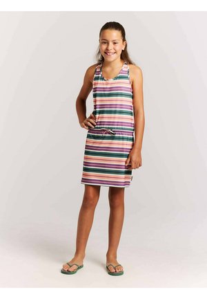 Mädchen steht mit der Hand in der Hüfte, trägt ein ärmelloses, knielanges Kleid mit horizontalen pinken, grünen, orange- und lilafarbenen Streifen und grünen Flip-Flops.