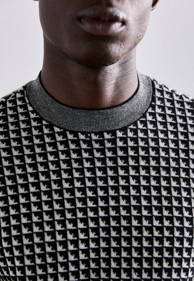 Pull en tricot noir et blanc à motif, présentant un design texturé avec un col noir côtelé. La vue en gros plan met en évidence le détail du tissu.