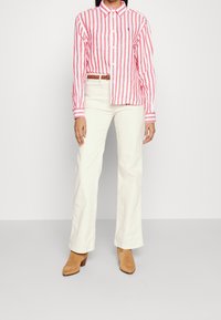 Camisa de rayas rojas y blancas de manga larga con cierre de botones, combinada con pantalones de pierna ancha color crema y botas de tacón color marrón.