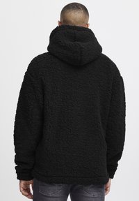 Black fleece hoodie with a textured, plush exterior and a large, relaxed hood. Features long sleeves and an oversized fit.