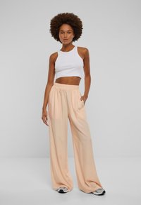 Licht perzikkleurige wijde broek gemaakt van een gladde stof met een elastische tailleband, gecombineerd met een witte cropped mouwloze top.