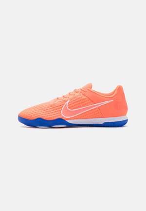 Chaussure de football indoor Nike orange vif avec logo swoosh blanc et tige texturée, dotée d'une semelle bleue et blanche.