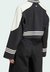 Černobílá krátká mikina se širokými rukávy, třemi bílými pruhy na manžetách a malým logem na zadním límci.