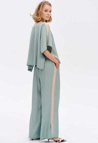Lichtgroene twee-delige outfit met een losse top met brede mouwen en wijde broek met een tan streep. Soepele, vloeiende textuur.
