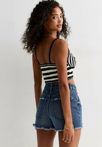 Randig svart-och-vit stickad crop top med tunna band, tillsammans med högmidjade slitna jeansshorts med fransade fållar och bakfickor.