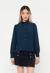 Bluză navy blue, cu mânecă lungă, cu închidere cu nasturi, guler clasic și țesătură texturată. Combinate cu o fustă închisă la culoare, cu nasturi argintii.