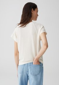 Korte mouwen, textuurrijke crèmekleurige top met een relaxte pasvorm, gecombineerd met lichtblauwe jeans, met een achterkant en zakdetails.