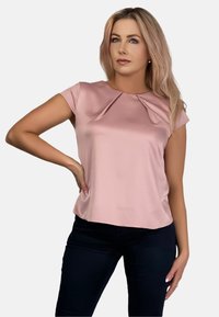 Krótki, różowy top z satyny z plisowanym dekoltem, gładką fakturą i luźnym krojem, zestawiony z ciemnymi, dopasowanymi spodniami.