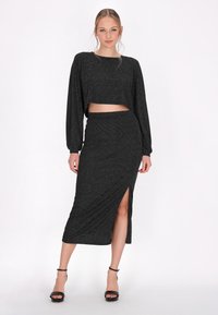Dwuczęściowy zestaw składający się z krótkiego czarnego topu z błyszczącymi detalami i dopasowanej midi spódnicy z bocznym rozcięciem, wykonany z elastycznego materiału.