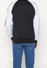 Černobílá raglánová mikina s černým tělem a bílými rukávy, s žebrovaným límcem a manžetami, nošená s modrými džíny.