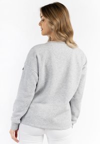 Felpa grigia con collo a giro e spalle scese, caratterizzata da una texture morbida. Vista posteriore con dettagli di cucitura curva.