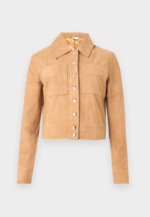 Lys beige semsketjakke med korte ermer, to frontlommer med klaff, sølvfargede trykknapper og spiss krage på hvit bakgrunn.