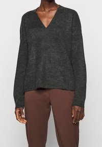 Dunkelgrauer, gestrickter Pullover mit V-Ausschnitt und langen Ärmeln. Verfügt über eine lockere Passform und einen leicht verkürzten Saum. Der Stoff hat eine weiche Textur.