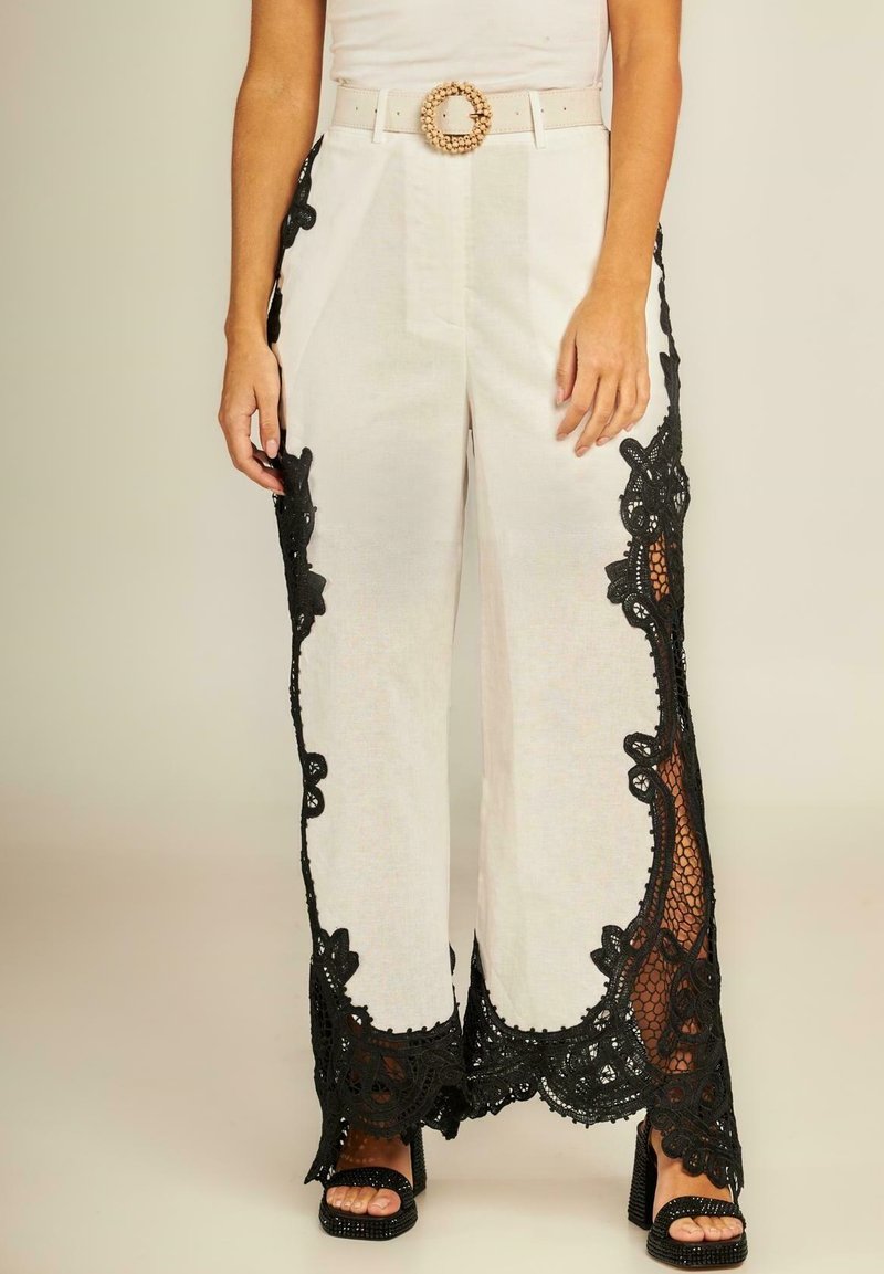 Witte wijde broek met zwarte kantaccenten langs de zijkanten, met een gestructureerde afwerking, en een witte riem met een ronde gespsluiting.