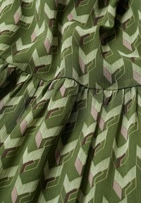 Tissu vert avec un motif géométrique de cubes imbriqués dans des tons de vert, marron et beige, avec un détail de couture froncée.