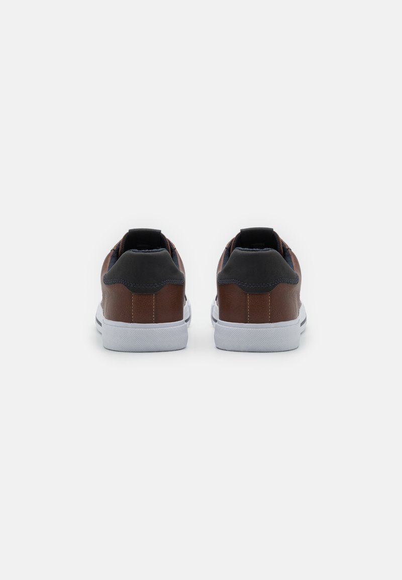 Baskets en cuir marron avec des accents noirs, semelles en caoutchouc blanc et une texture lisse. Elles présentent un bout arrondi et un col rembourré.
