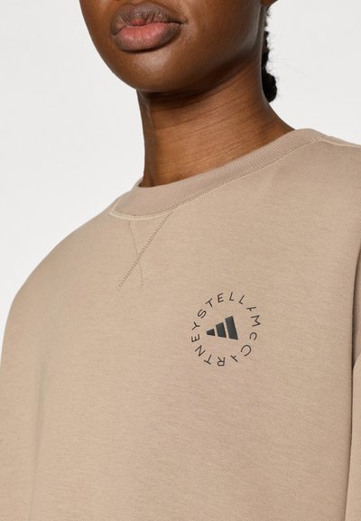 Μπεζ φούτερ με στρογγυλό λογότυπο και μαύρες λεπτομέρειες. Διαθέτει ριμπ λαιμόκοψη και εμφανή ραφή. Ομαλή υφή.