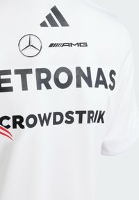 Bijela sportska majica s crnim logotipima Petronas, CrowdStrike i AMG, s crno-crvenim grafičkim naglascima. Mekani, sintetički materijal.
