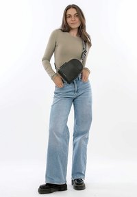 Černá kožená crossbody taška s zaoblen�ým vrchem, texturovaným povrchem a nastavitelným popruhem, nošená přes taupe dlouhý rukáv top a modré široké džíny.
