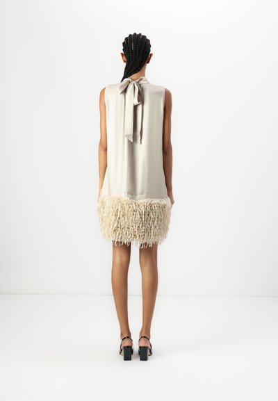 Robe sans manches en beige clair avec un ourlet à franges texturé. Comprend un détail de lien dans le dos, et la jupe a une apparence douce et shaggy.