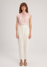 Blusa rosa con motivo floreale e scollatura arricciata, abbinata a pantaloni crema a vita alta e scarpe marrone chiaro. Tessuto morbido e vestibilità comoda.