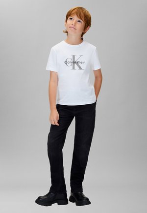 Wit katoenen T-shirt met een zwart "Calvin Klein" logo, gecombineerd met zwarte spijkerbroek en zwarte enkellaarsjes. Eenvoudig ontwerp, casual pasvorm.
