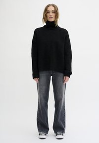 Schwarzer Strickrollkragenpullover kombiniert mit grauen Jeans. Der Stoff wirkt weich und hat eine lässige Passform, mit langen Ärmeln und weit geschnittenen Beinen.