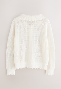 Baltas megztinis su ilgomis rankovėmis, briaunuotu apykakliu ir rankogalais bei bangelėmis suformuotu apdailos kraštu, parodytas iš nugaros šviesiame fone.