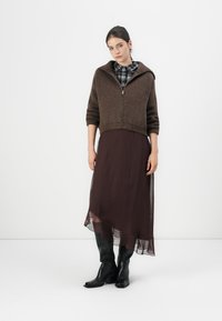 Brun strikket zippered cardigan med en cropped design, parret med en semitransparent burgunder lagdelt kjole og svarte knelang støvler.