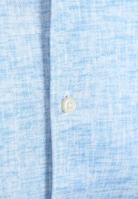 Lichtblauw geweven stoffen shirt met een knoopsluiting. Het materiaal heeft een zachte textuur en een subtiel patroon, wat het casual ontwerp benadrukt.