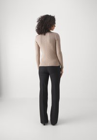 Beige ribbet langærmet top med fitted design, parret med sorte skræddersyede bukser. Outfitet har en glat tekstur og minimalisk stil.