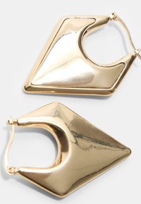 Geometriska creoler i guldfärg med en polerad metallisk yta, med triangulär form och en cirkulär utskuren detalj.