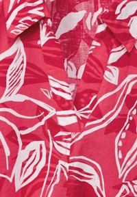 Tissu rouge avec des motifs de feuilles abstraites blancs, dotée d'un col en V et de détails de couture visibles.