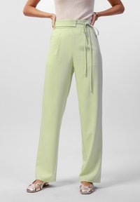 Lichtgroene, hooggeplaatste broek met een strikceintuur, met een wijde pijpontwerp en een gladde textuur. Gepaard met metallic instappers.