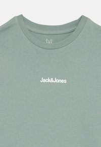 Žalias medvilnės marškinėliai su apvaliu iškirpimu ir balta "Jack&Jones" logo. Lygi tekstūra, kasdieniškas siluetas ir minimalus dizainas.