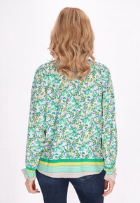 Camicia a maniche lunghe con bottoni, caratterizzata da un motivo floreale multicolore, tessuto leggero e un orlo a strati con una finitura a righe nella parte inferiore.