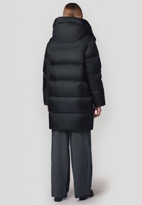 Czarna kurtka puchowa z wysokim kołnierzem, pikowanym wzorem i długimi rękawami. Ma luźny fason i długość do połowy uda.